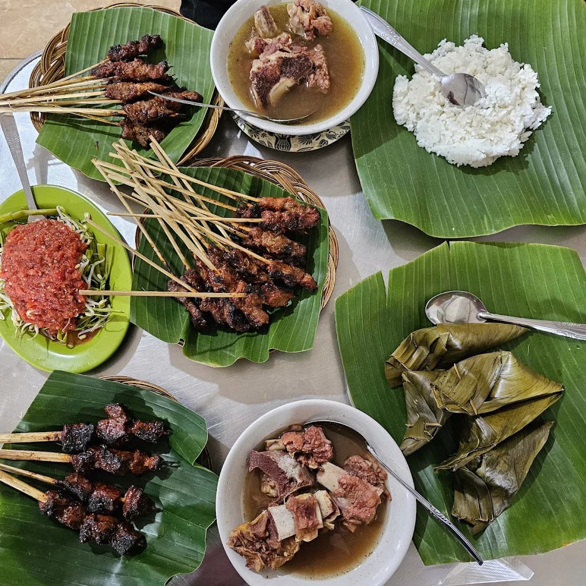 Sate, kuah, dan pelengkap di atas daun pisang
