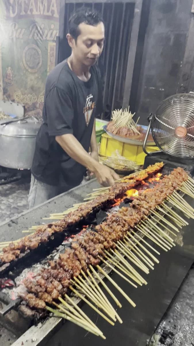 Juru bakar membolak-balik puluhan tusuk sate di atas bara arang