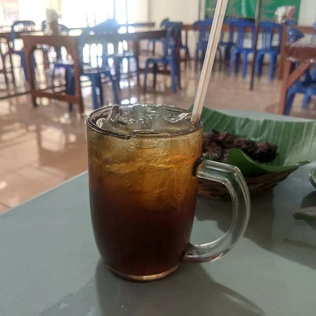Meja makan warung dengan es teh dan sate di atas daun pisang